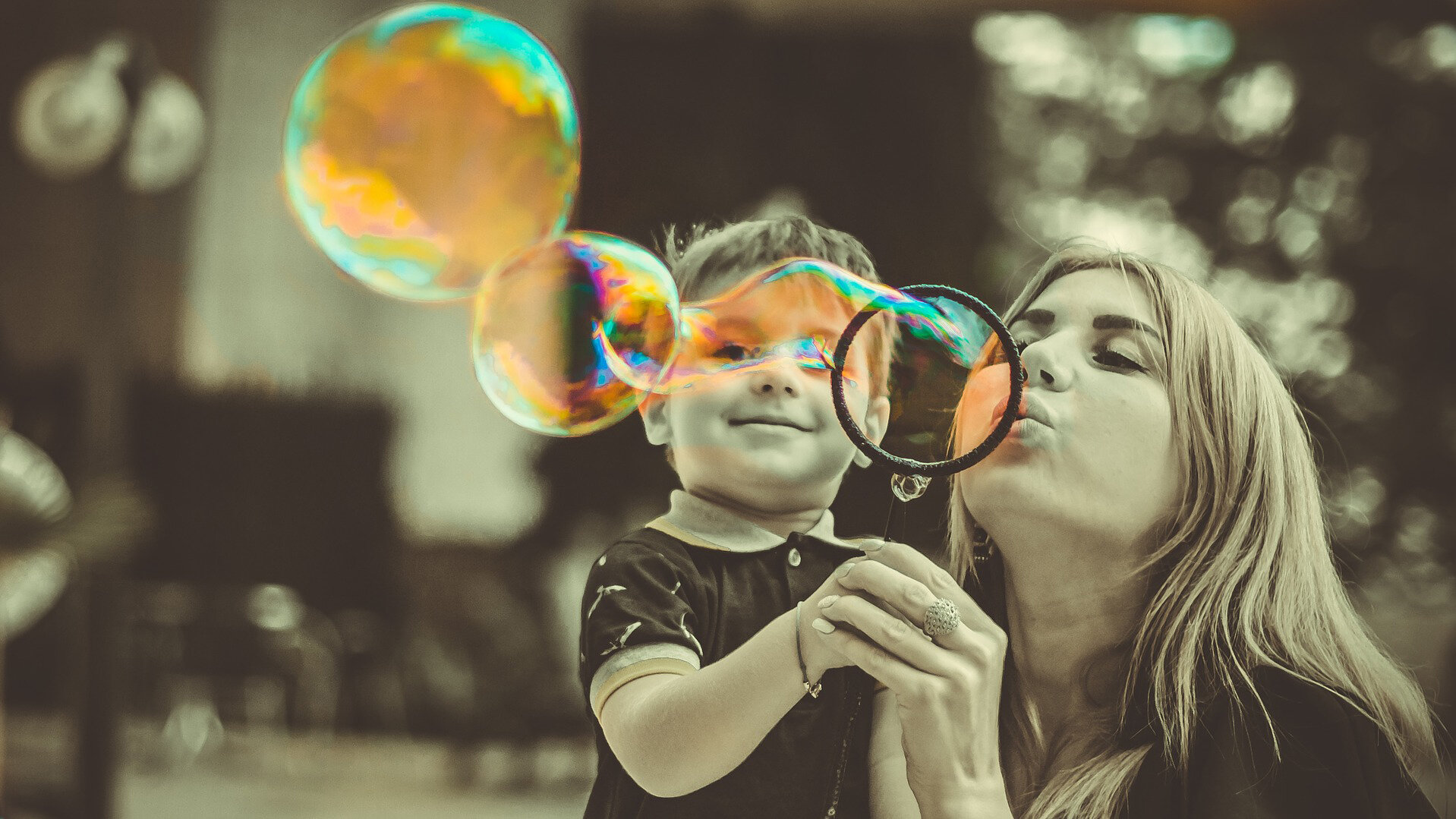 Frau mit Kind macht bunte Seifenblasen / Woman with child making colourful soap bubbles