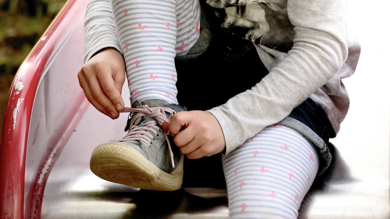 Mädchen auf einer Rutsche bindet sich ihren Schuh zu / Girl on a slide tying her shoe
