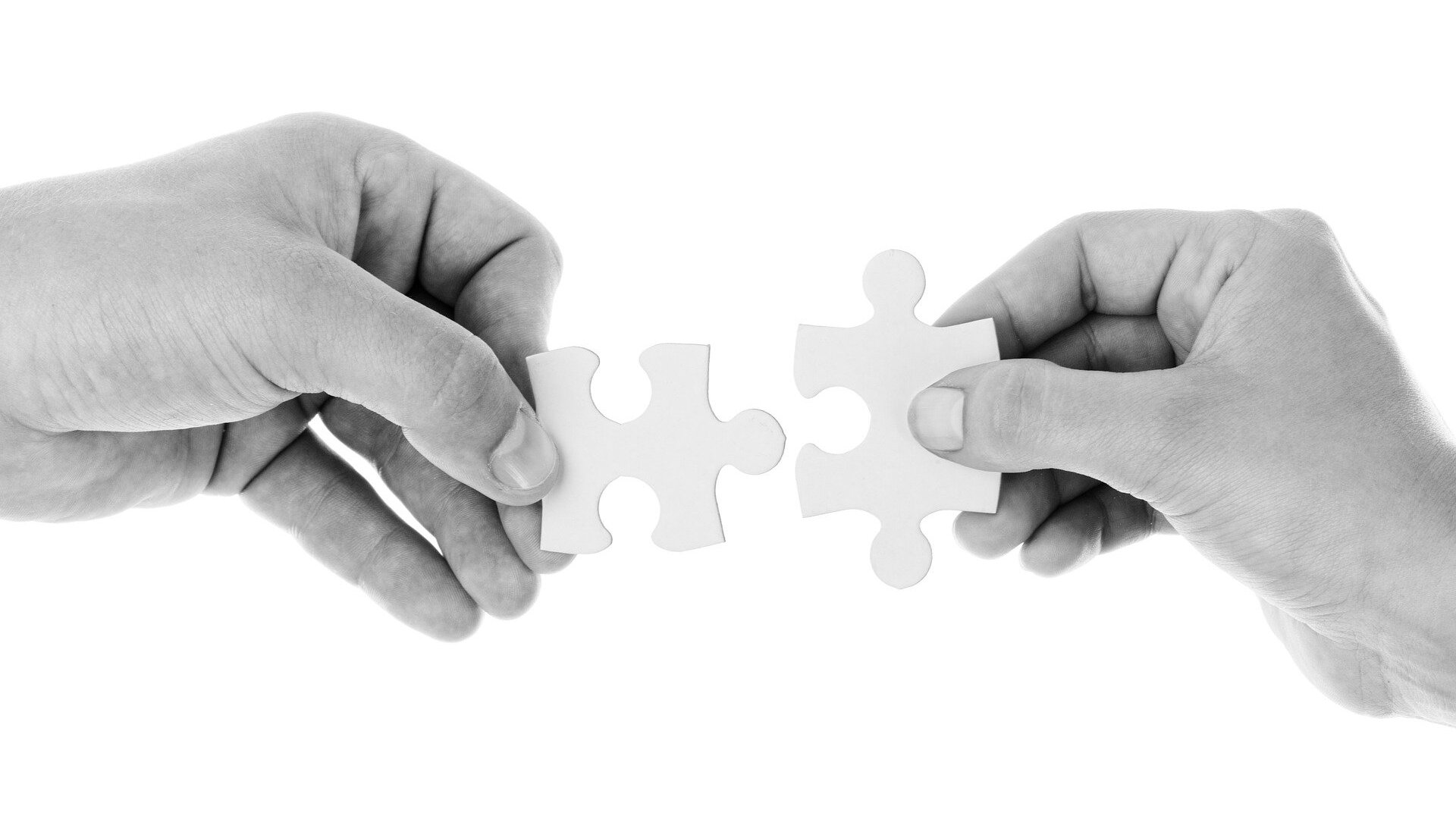 Zwei Hände fügen zwei Puzzleteile zusammen / Two hands putting two pieces of a puzzle together