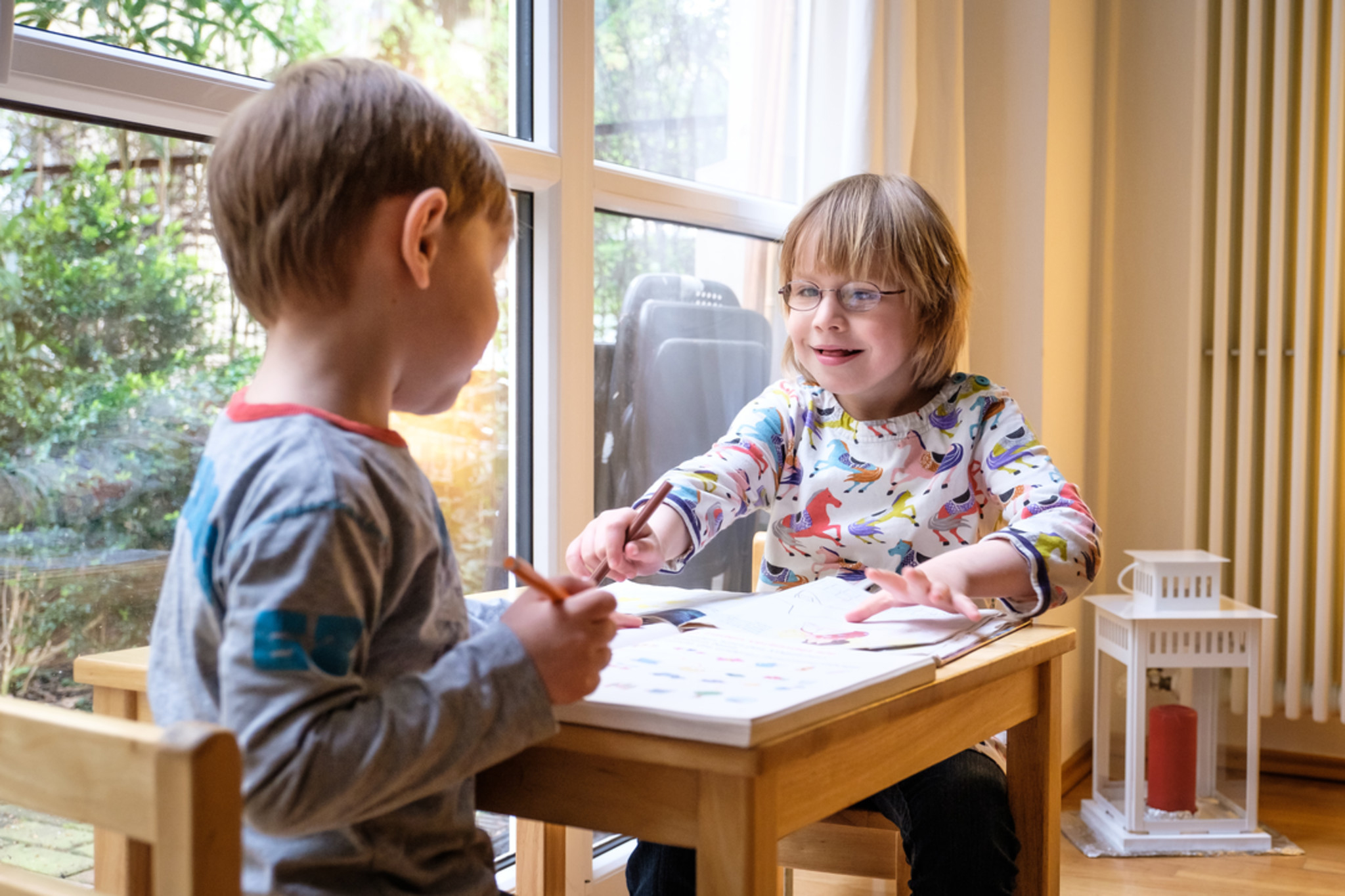 Alltag in einer Familie mit behinderten und nicht behinderten Kindern: Zwei Kinder sitzen an einem Tisch und malen / Everyday life in a family with disabled and non-disabled children: Two children sitting at a table and drawing
